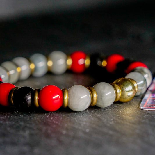 Close-up of a beaded bracelet with red, gray, and gold beads on a dark surface.